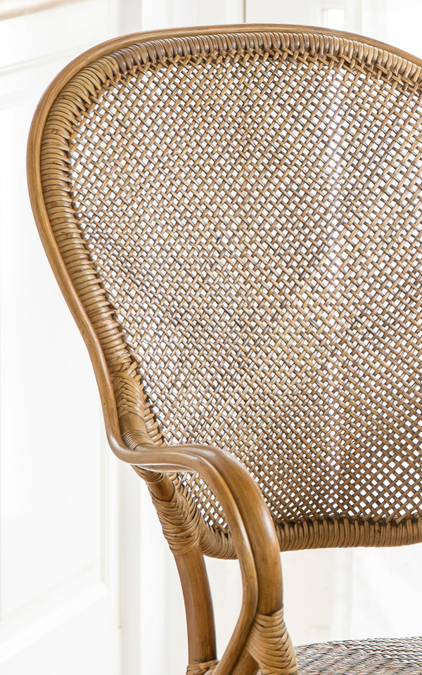 Esta es una imagen de detalle de Rossini sillón de comedor en antique rattan. Detalle del reposabrazos curvo de ratán, asiento tejido y uniones envueltas.