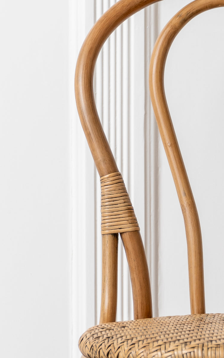 Esta es una imagen de detalle de Lulu silla de comedor en antique rattan. El marco curvado de madera con envoltura de ratán y asiento tejido destacan el diseño.