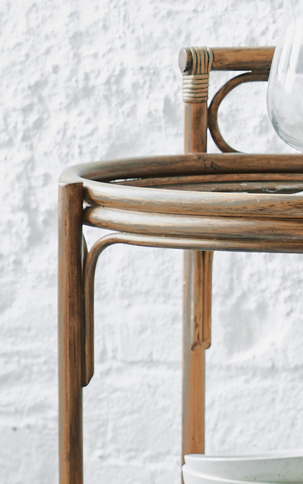 Esta es una imagen de detalle de Romeo carrito en antique rattan. Detalle de la estructura redonda del carrito de ratán sobre una pared de ladrillo blanco.