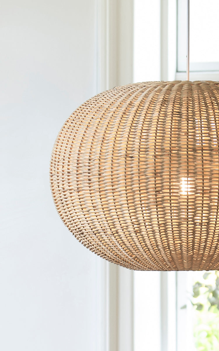Esta es una imagen de detalle de Tangelo Lampshade Ø62 cm | Large en natural rattan. Detalle del tejido grande de ratán de la lámpara colgante redondeada junto a una ventana.