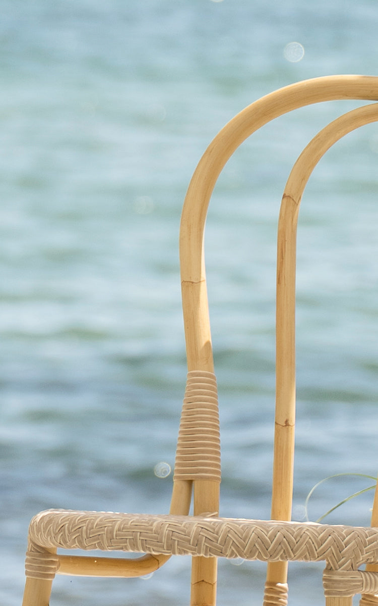 Esta es una imagen de detalle de Lulu silla de comedor exterior en natural aluminium artfibre. El marco curvado y el detalle tejido se muestran junto al mar.