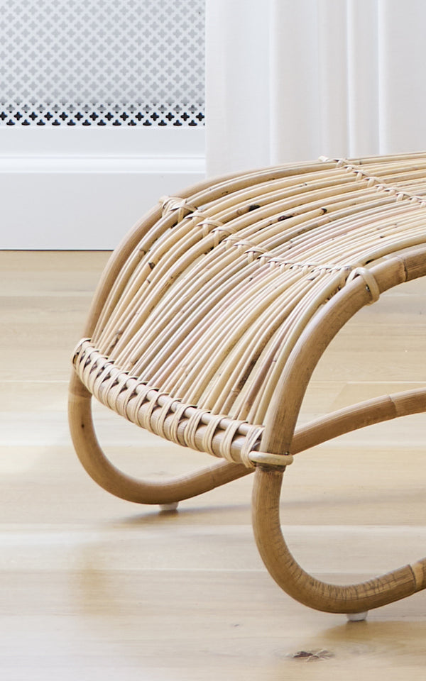 Esta es una imagen de detalle de Teddy reposapiés en polished natural rattan. Detalle de las molduras curvas de ratán y envoltorio trenzado del reposapiés.