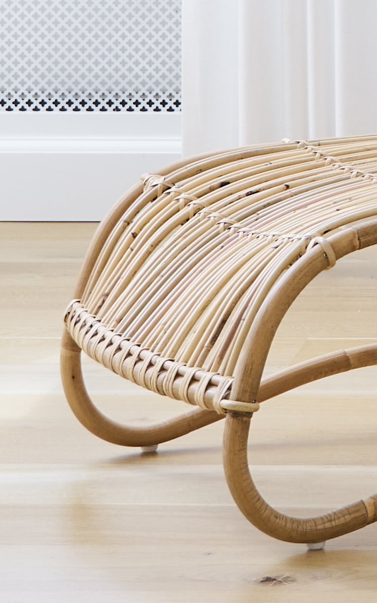 Esta es una imagen de detalle de Teddy reposapiés en polished natural rattan. Detalle de las molduras curvas de ratán y envoltorio trenzado del reposapiés.