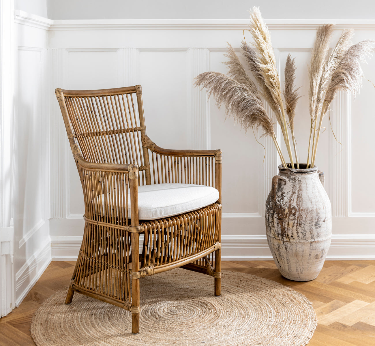 Esta es una imagen de estilo de vida de Davinci silla de comedor en antique rattan, en un interior luminoso con paredes de paneles blancos y parqué.
