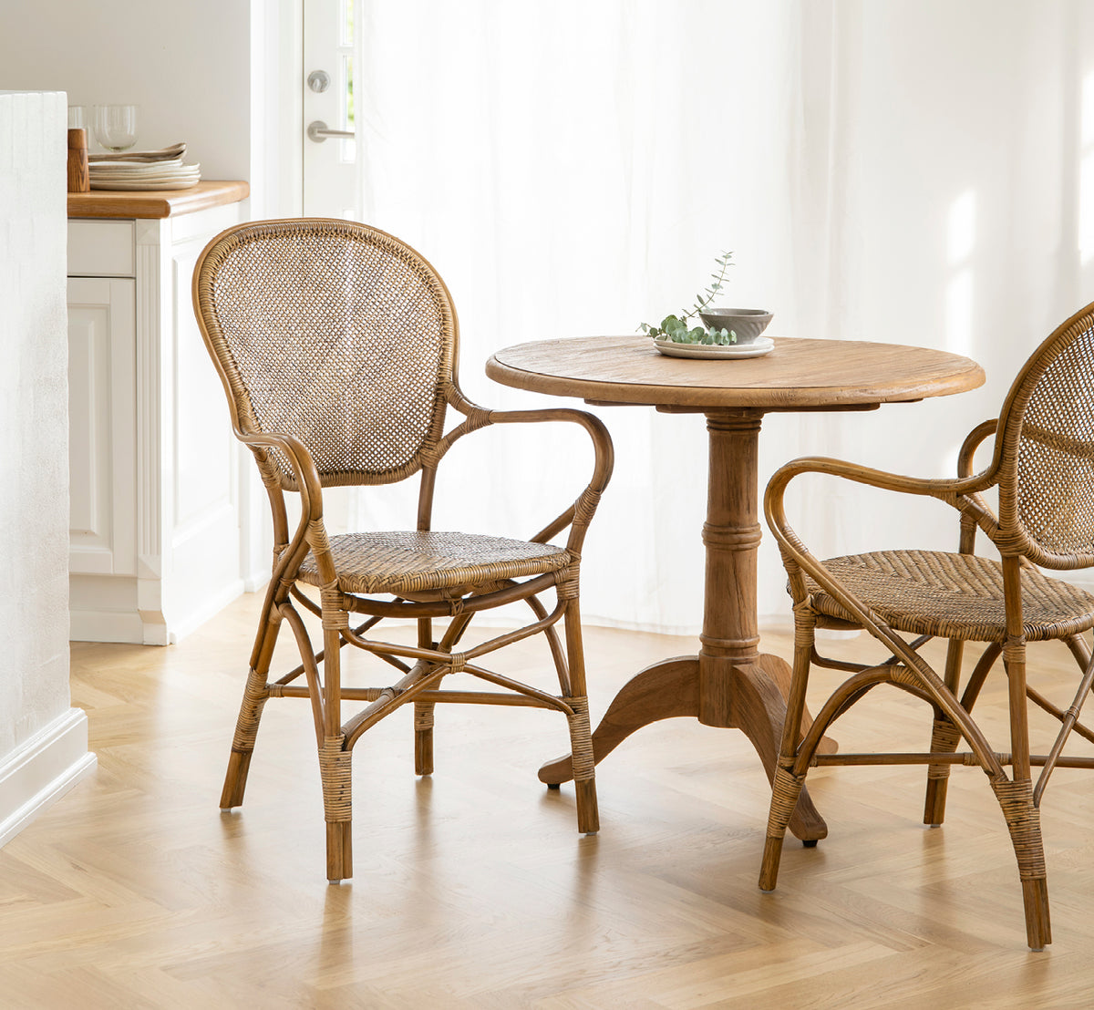 Esta es una imagen de estilo de vida de Rossini sillón de comedor en antique rattan. Combinado con una mesa de café redonda en un interior escandinavo luminoso y aireado.