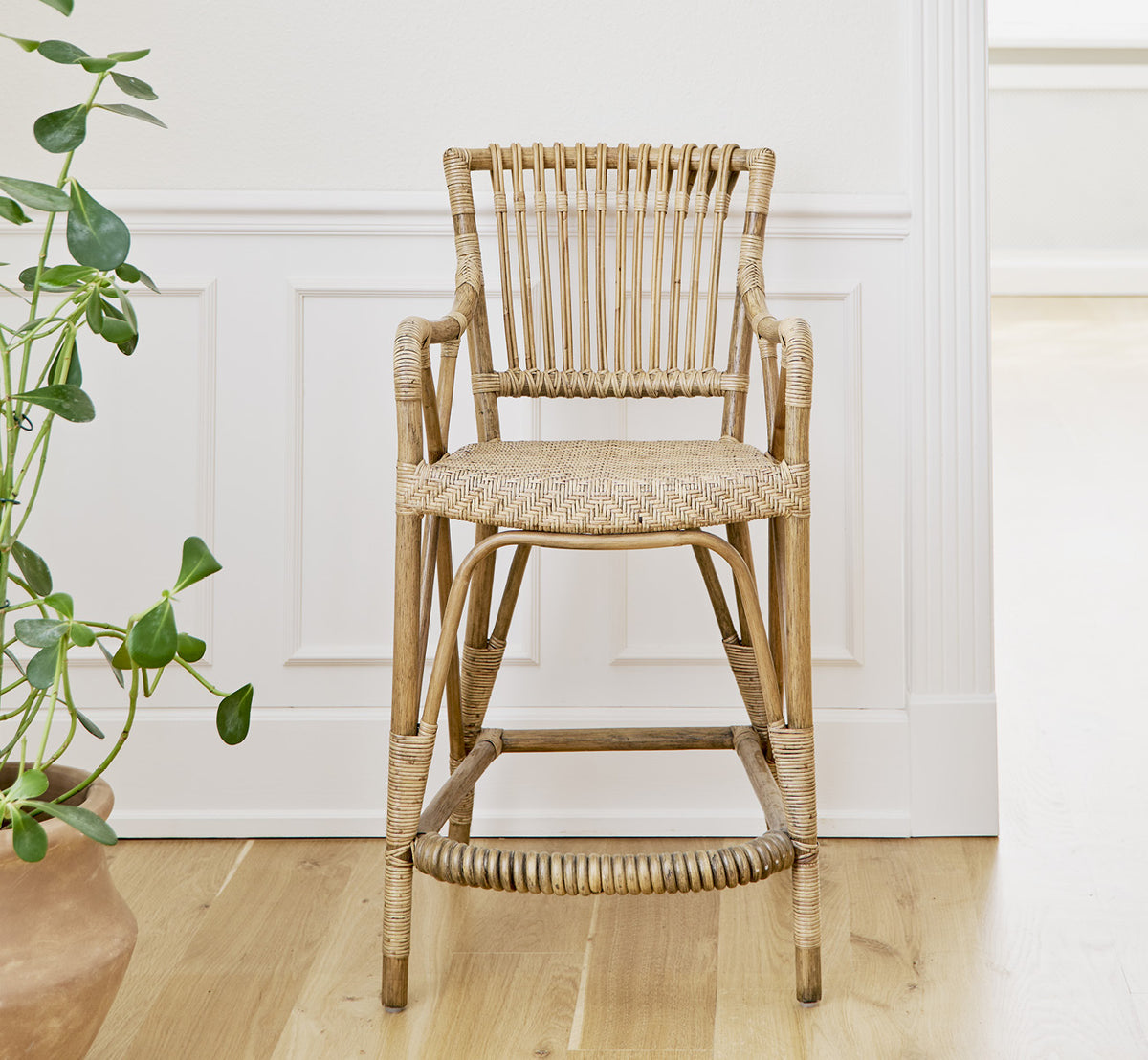 Esta es una imagen de estilo de vida de Blues taburete alto en antique Rattan, en un interior luminoso con paredes de paneles blancos y parqué en.