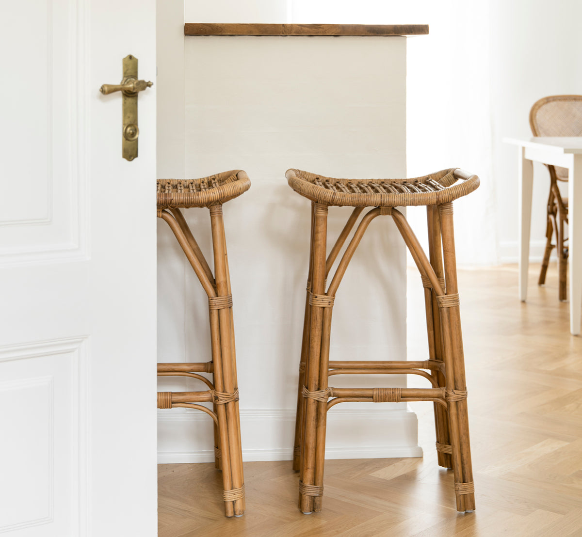 Esta es una imagen de estilo de vida de Salsa taburete de bar en antique rattan. Un par colocadas contra una pared blanca sobre suelo de parqué en espiga.