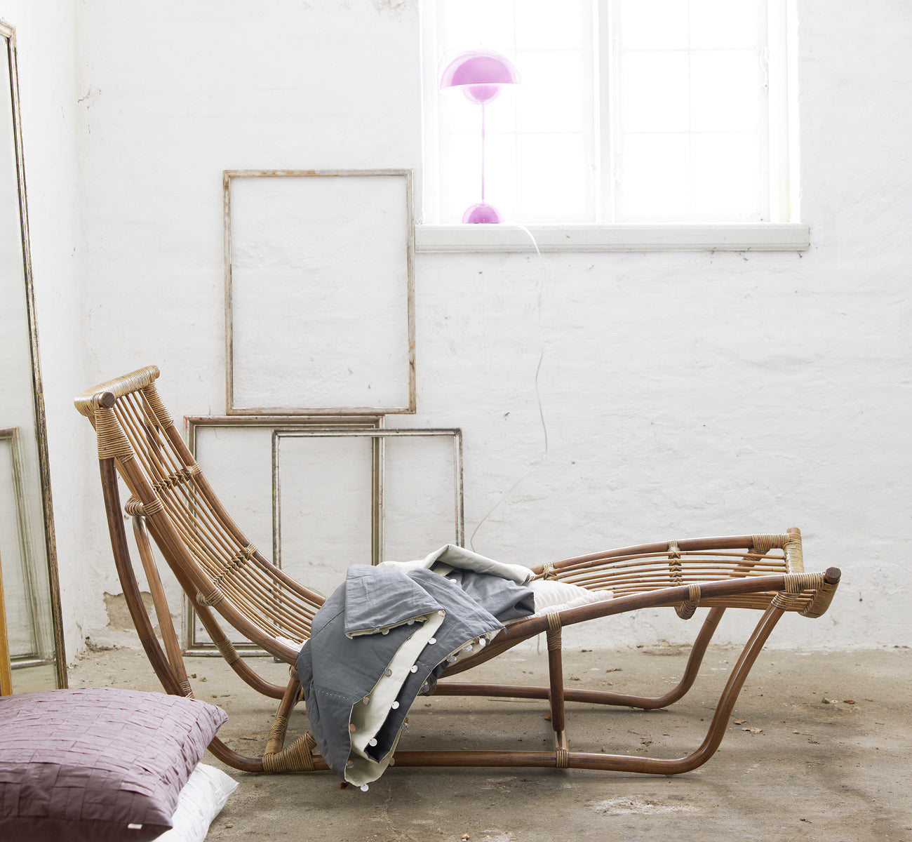 Esta es una imagen de estilo de vida de Michelangelo Daybed i antique rattan. Estilizado con mantas de lino en un estudio blanco con marcos vintage.