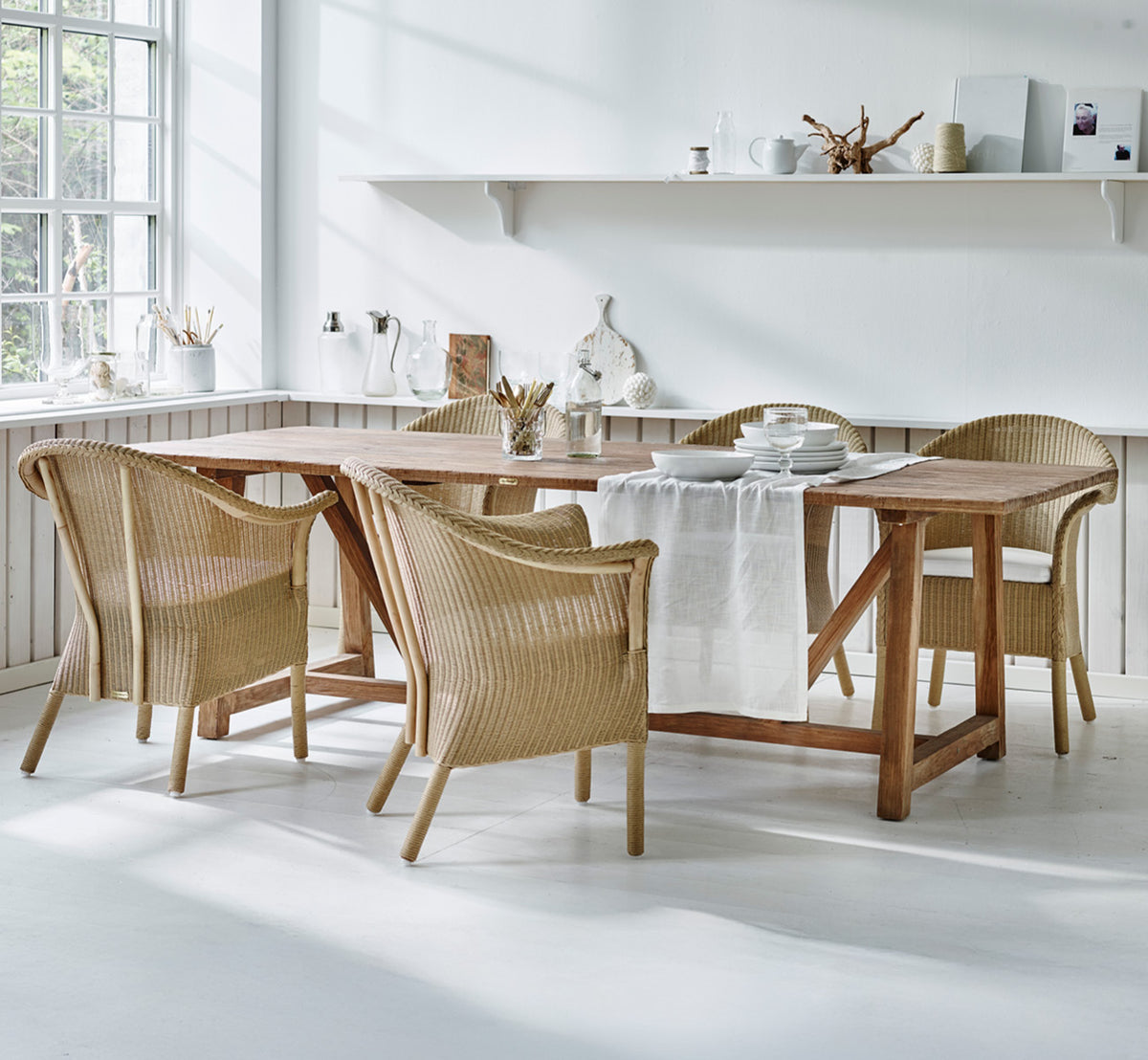 Esta es una imagen de estilo de vida de Classic silla de comedor en natural Loom Rattan Frame, en un interior luminoso con paredes de paneles blancos.