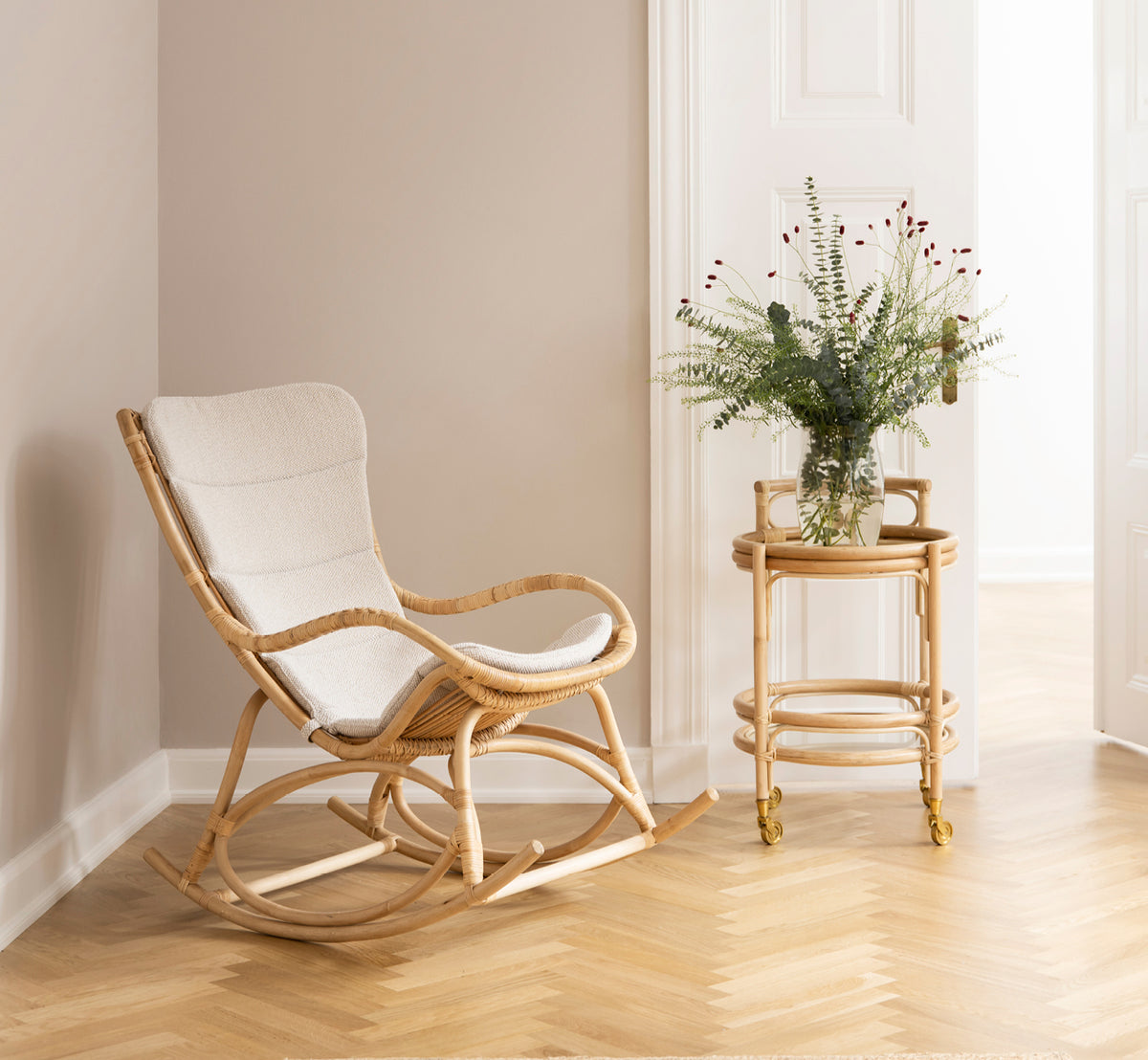 Esta es una imagen de estilo de vida de Monet Rocking Chair i natural rattan. En una habitación con paredes rosa, parqué en espiga y eucalipto.