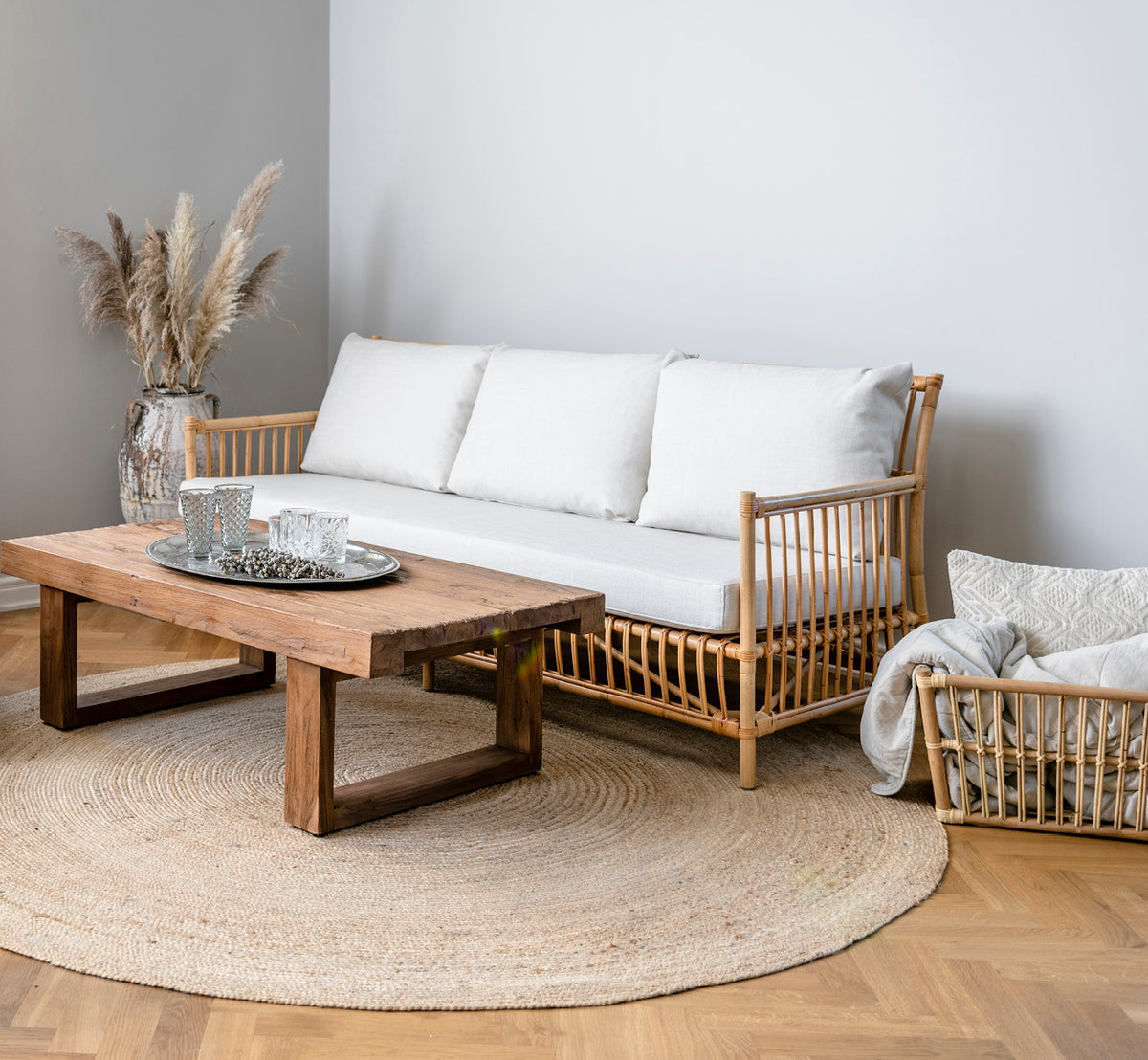 Esta es una imagen de estilo de vida de Caroline sofá en natural rattan, en un interior luminoso con paredes de paneles blancos y parqué en espiga.