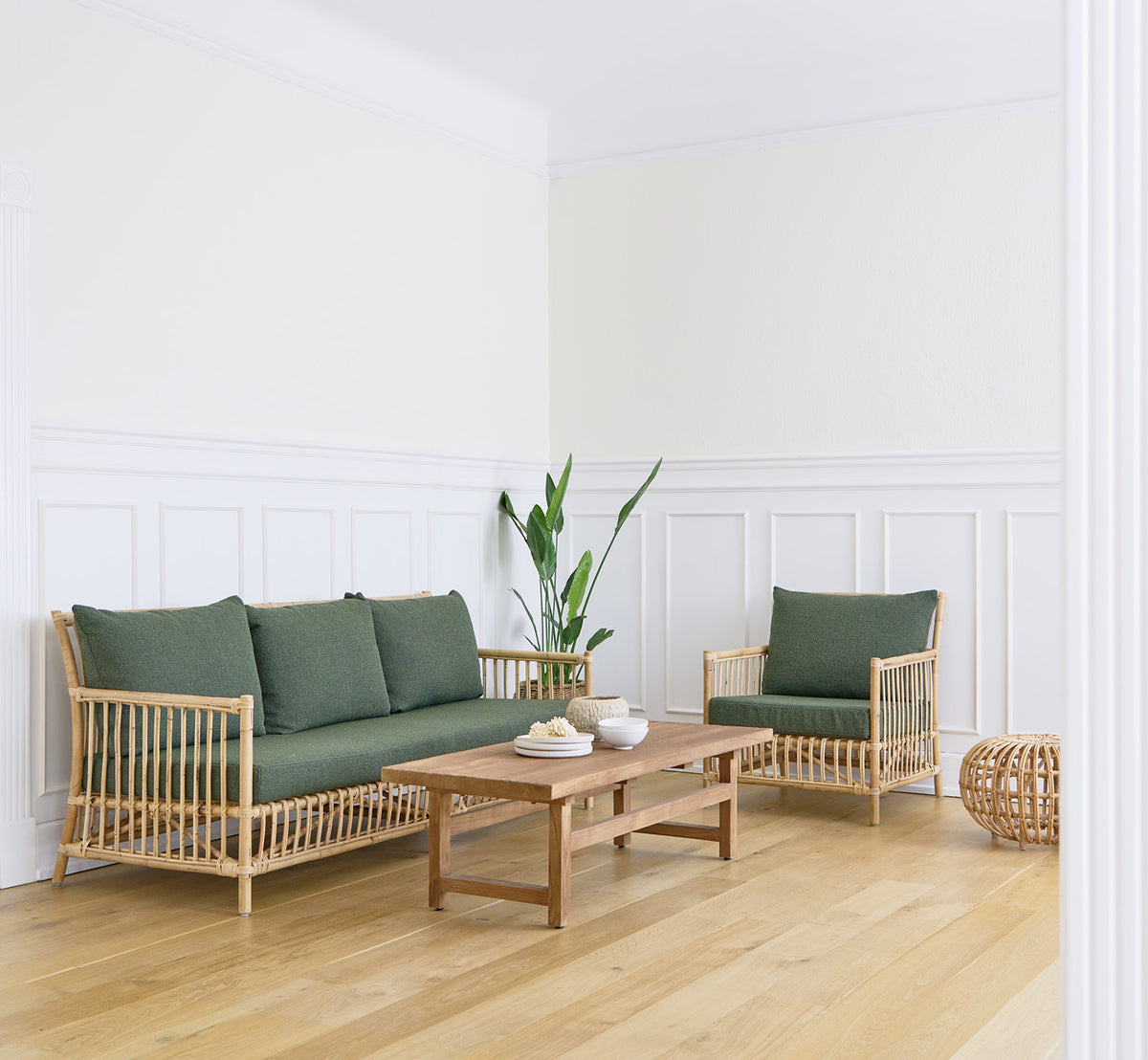 Esta es una imagen de estilo de vida de Caroline sofá en natural rattan, en un interior luminoso con paredes de paneles blancos y parqué en espiga.