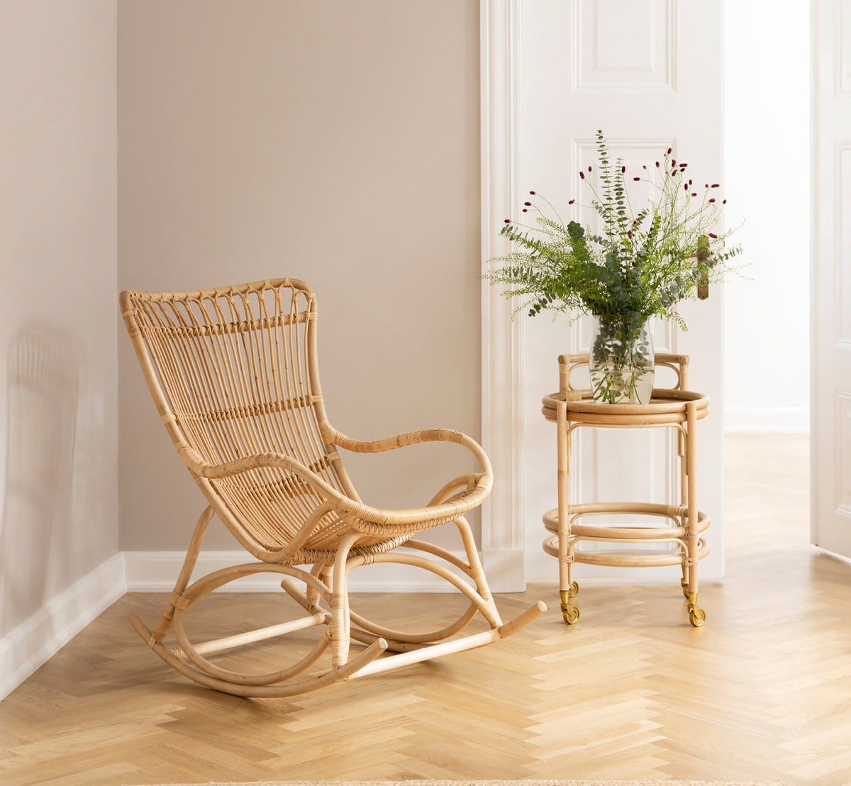 Esta es una imagen de estilo de vida de Romeo Trolley i natural rattan. Estilizado con vasos en un rincón acogedor con suelo de parqué en espiga.