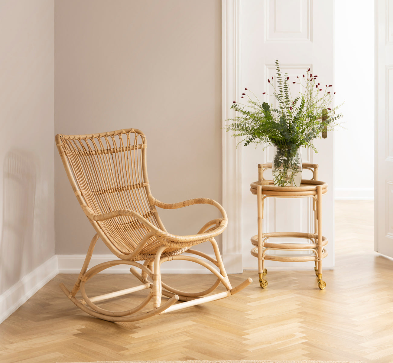 Esta es una imagen de estilo de vida de Romeo Trolley i natural rattan. Estilizado con vasos en un rincón acogedor con suelo de parqué en espiga.