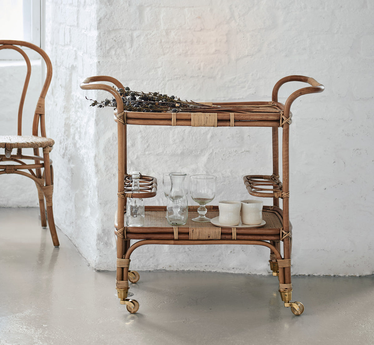 Esta es una imagen de estilo de vida de Carlo Trolley en antique Rattan, en un interior blanco y luminoso con revestimiento de pared y espejo de.