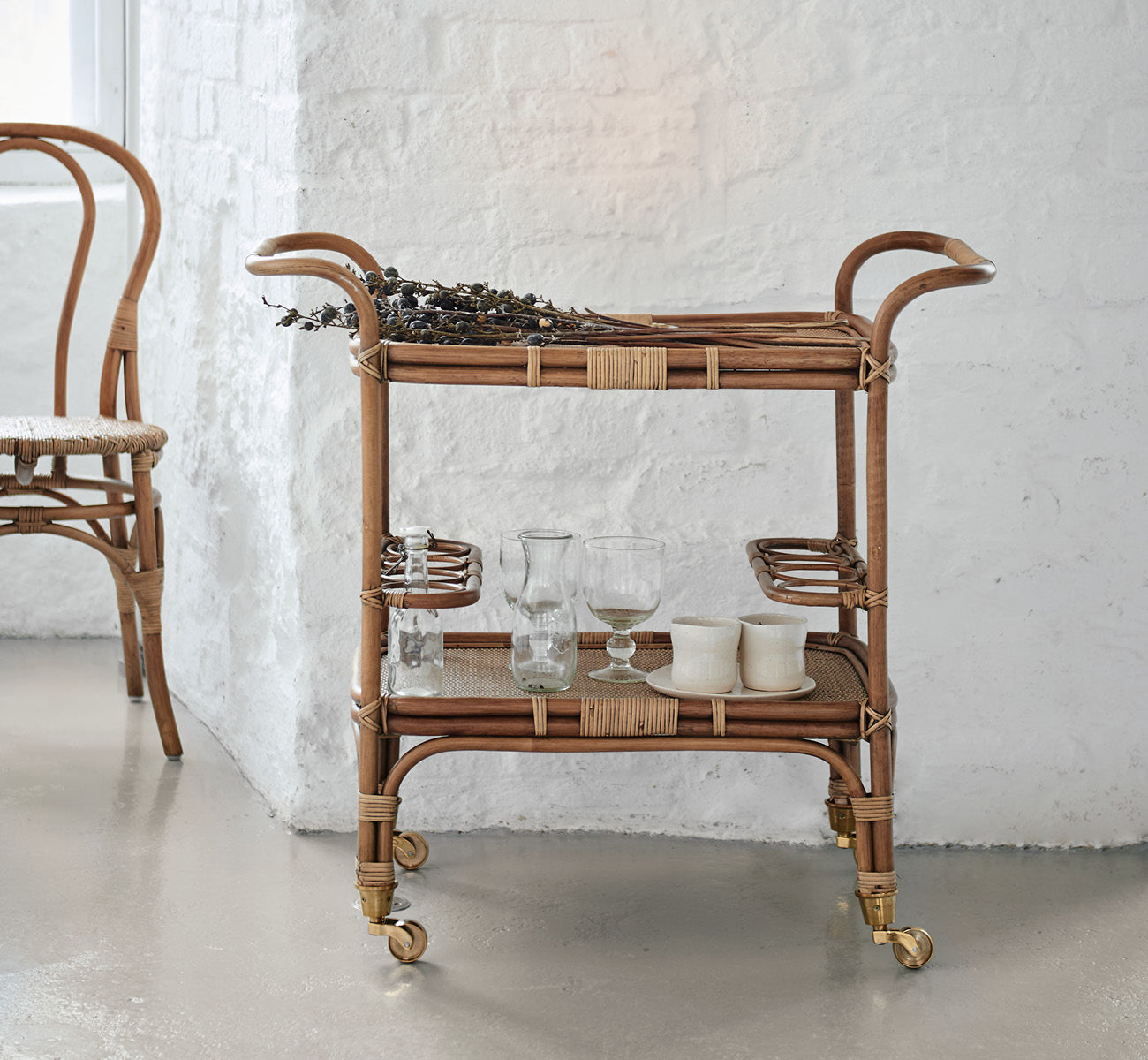 Esta es una imagen de estilo de vida de Carlo Trolley en antique Rattan, en un interior blanco y luminoso con revestimiento de pared y espejo de.