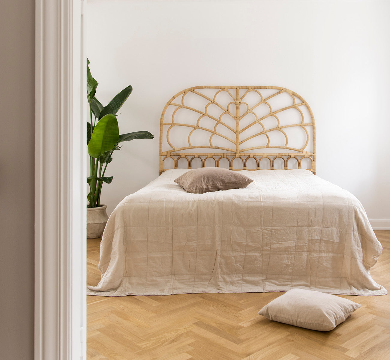 Esta es una imagen de estilo de vida de Celia cabecero en natural rattan, en un dormitorio tranquilo y luminoso con ropa de cama neutra y parqué en.