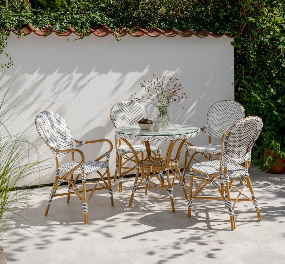 Esta es una imagen de estilo de vida de Isabell sillón de comedor exterior en almond aluminium frame white w cappuccino dot artfibre. En una terraza soleada.