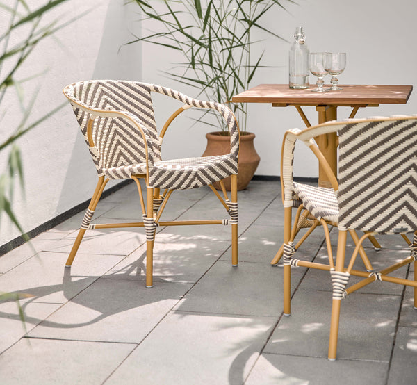 Esta es una imagen de estilo de vida de Madeleine silla de comedor exterior en almond aluminum frame chevron cappuccino ivory ArtFibre. Terraza soleada con mesa de teca.