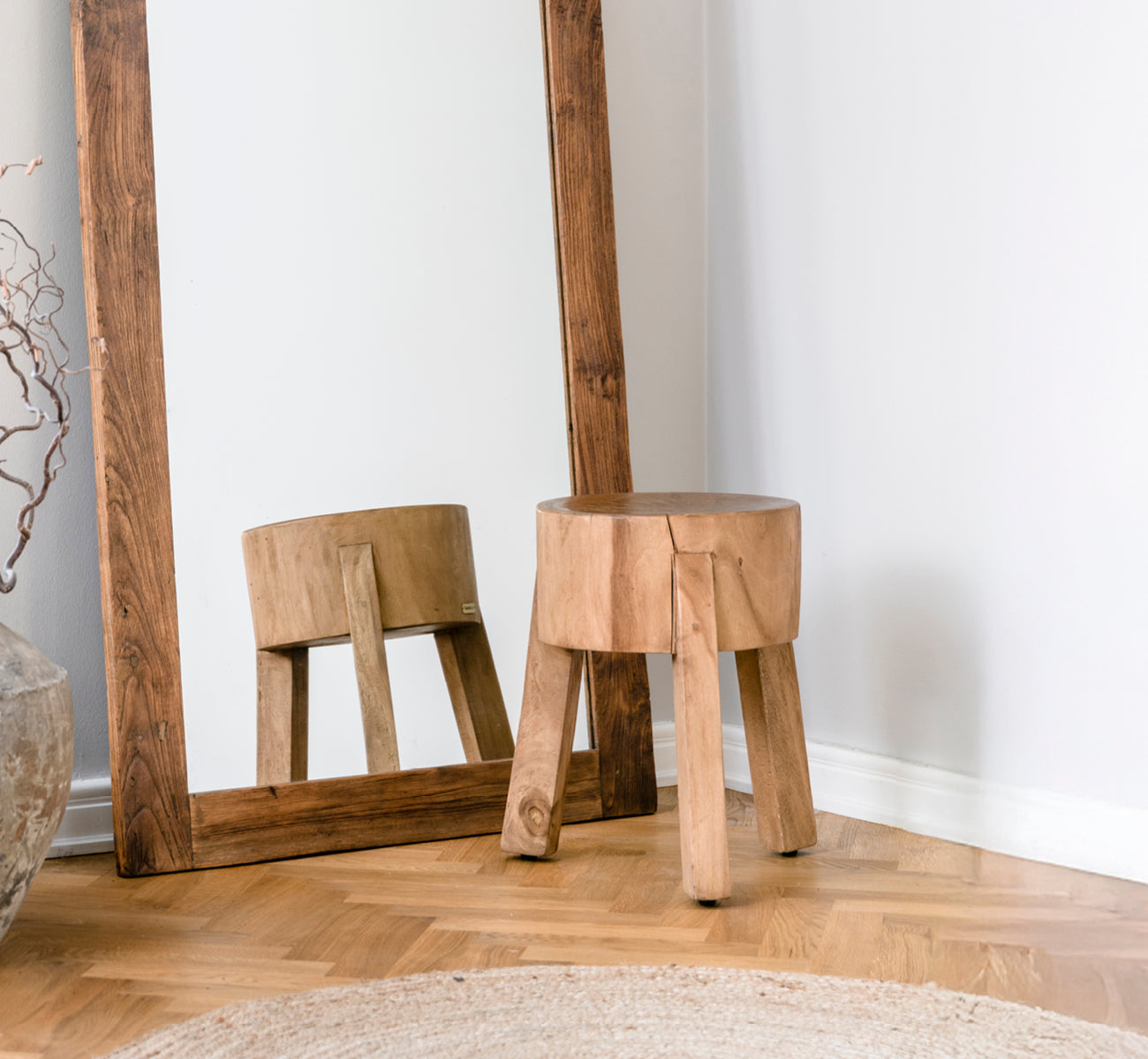 Esta es una imagen de estilo de vida de Roger taburete en teak indoor. Colocada junto a un escritorio de madera con lámpara y planta en un estudio luminoso con suelo en espiga.