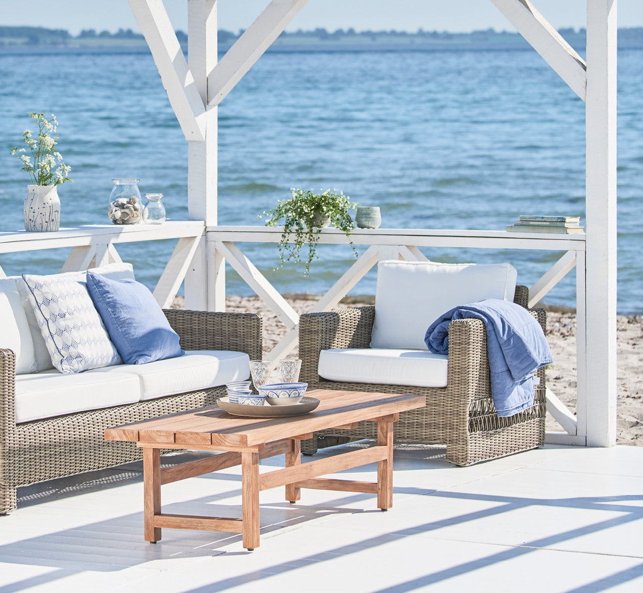 Esta es una imagen de estilo de vida de Carrie sillón lounge en antique Grey ArtFibre Aluminium, en una terraza costera soleada con vistas al mar y.