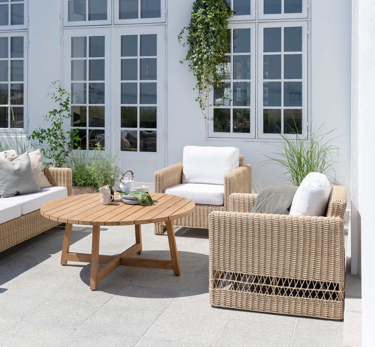 Esta es una imagen de estilo de vida de Carrie sillón lounge en natural ArtFibre Aluminium, en una terraza costera soleada con vistas al mar y.