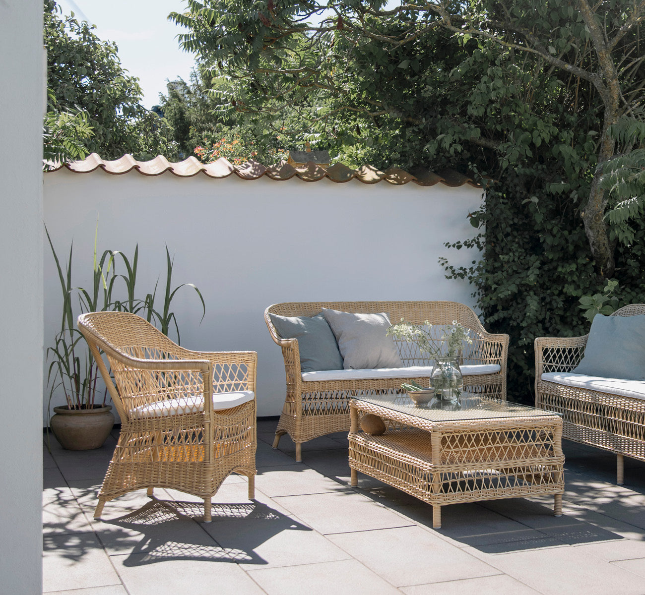 Esta es una imagen de estilo de vida de Charlot silla en natural ArtFibre Aluminium, en una terraza costera soleada con vistas al mar y una pérgola.