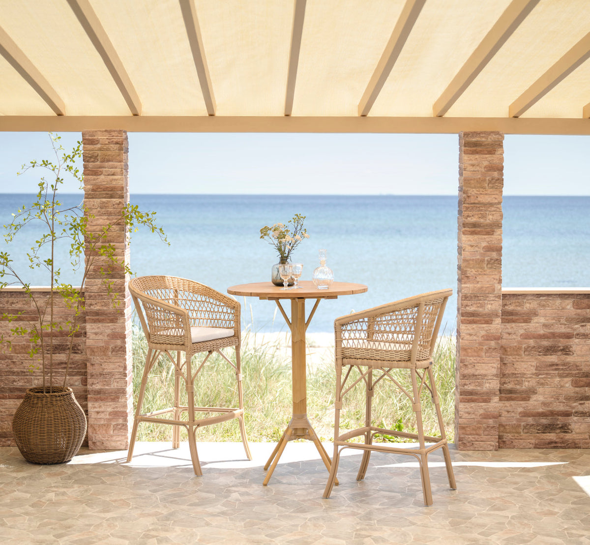 Esta es una imagen de estilo de vida de Emma taburete de bar exterior en natural artfibre aluminium. Conjunto de bar en una terraza junto al mar.
