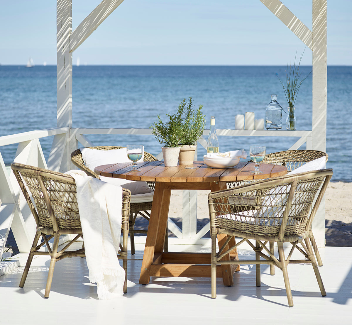 Esta es una imagen de estilo de vida de Emma silla de comedor exterior en antique Grey ArtFibre Aluminium, en una terraza costera luminosa con techo.