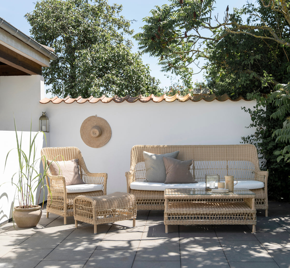 Esta es una imagen de estilo de vida de Dawn sofá en natural ArtFibre Aluminium, en una terraza costera con cubierta de madera blanca y vistas al mar.