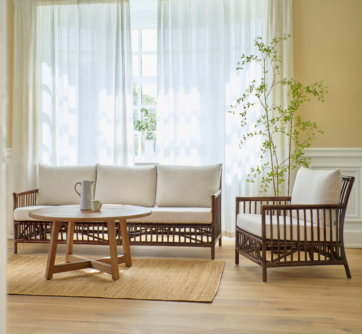 Esta es una imagen de estilo de vida de Aksel mesa de centro Ø100 cm en teak indoor. Con sofá de ratán y sillón lounge en una sala luminosa.