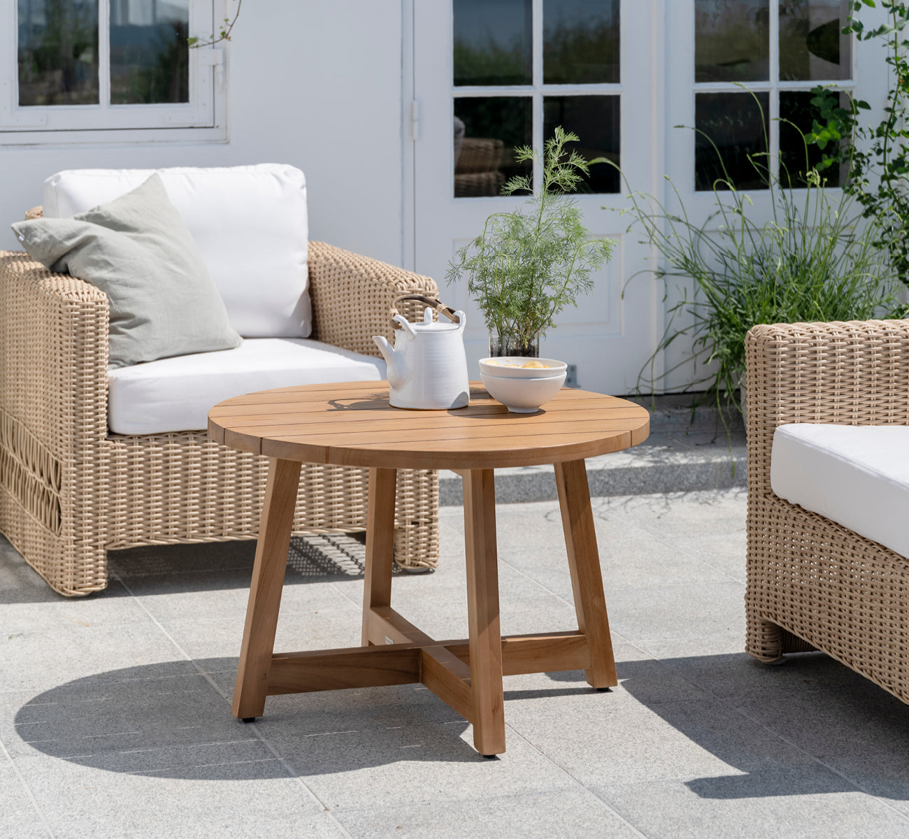 Esta es una imagen de estilo de vida de Victor Teak Lounge Table Ø75 cm en teak outdoor. Colocada en una terraza junto al mar entre divanes con cojines a rayas.
