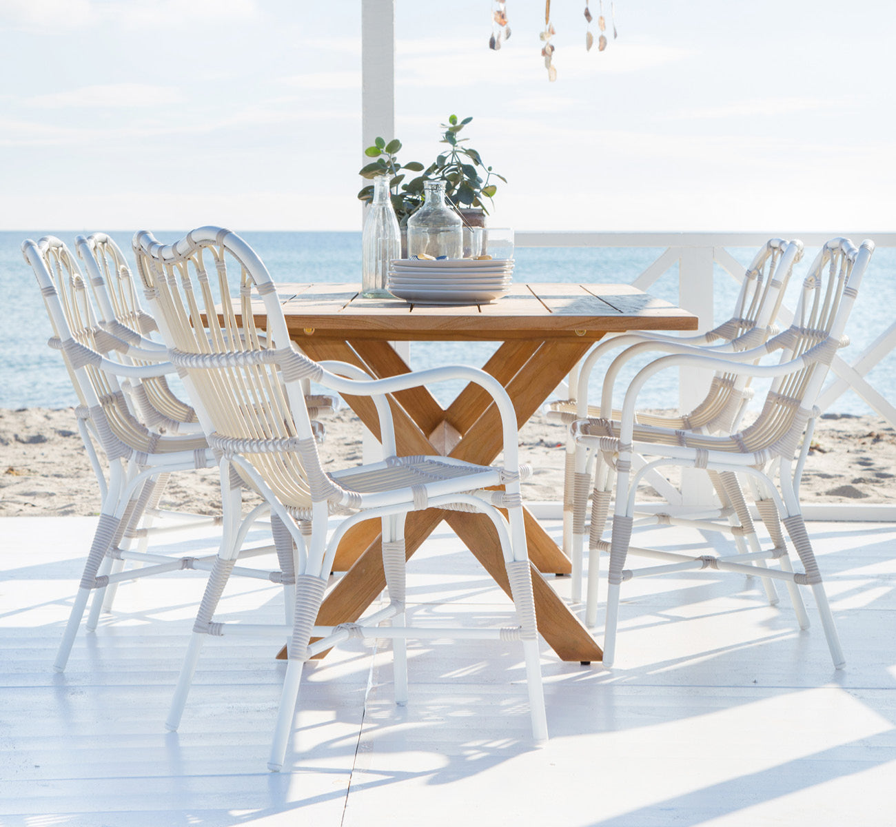 Esta es una imagen de estilo de vida de Colonial mesa 160 en outdoor Teak, en una terraza junto a la playa con cubierta de madera blanca y vistas al.