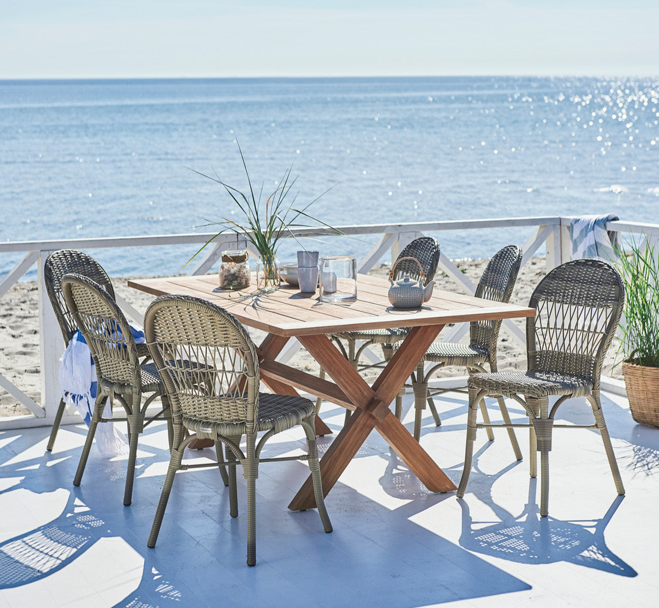 Esta es una imagen de estilo de vida de Colonial mesa 160 en outdoor Teak, en una terraza junto a la playa con cubierta de madera blanca y vistas al.