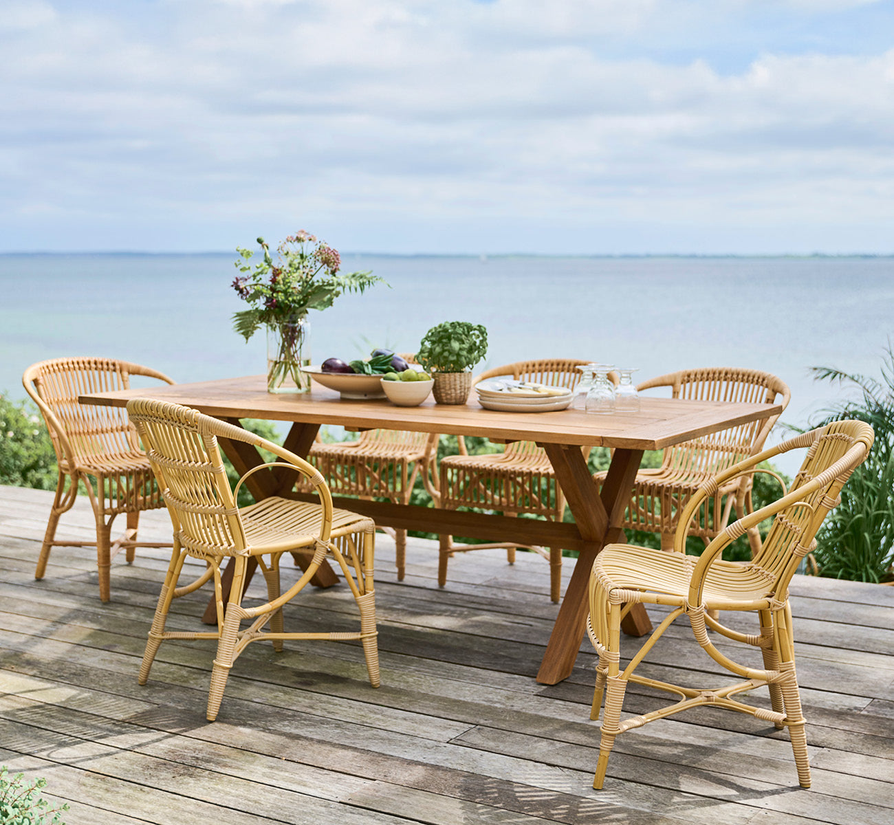 Esta es una imagen de estilo de vida de Colonial mesa 200 en outdoor Teak, en una terraza junto a la playa con cubierta de madera blanca y vistas al.