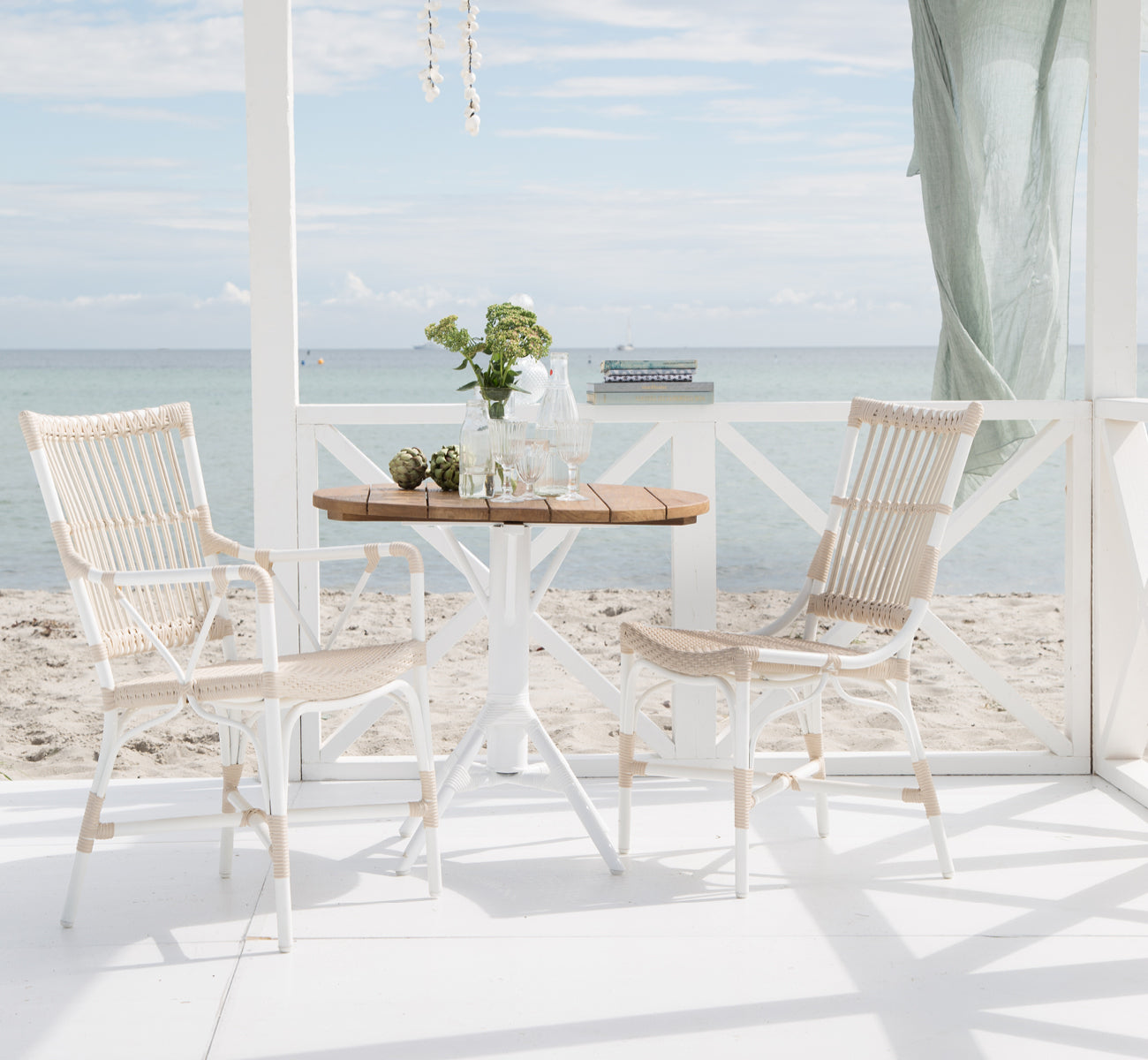 Esta es una imagen de estilo de vida de Nicole Cafe Table i white aluminium frame white ArtFibre. Con sillas Piano en una terraza junto al mar.