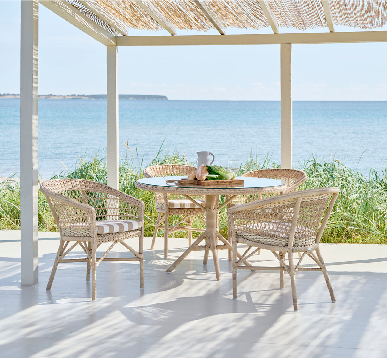 Esta es una imagen de estilo de vida de Grace mesa de comedor exterior en natural ArtFibre Aluminium, en un exuberante patio de jardín con suelo de.