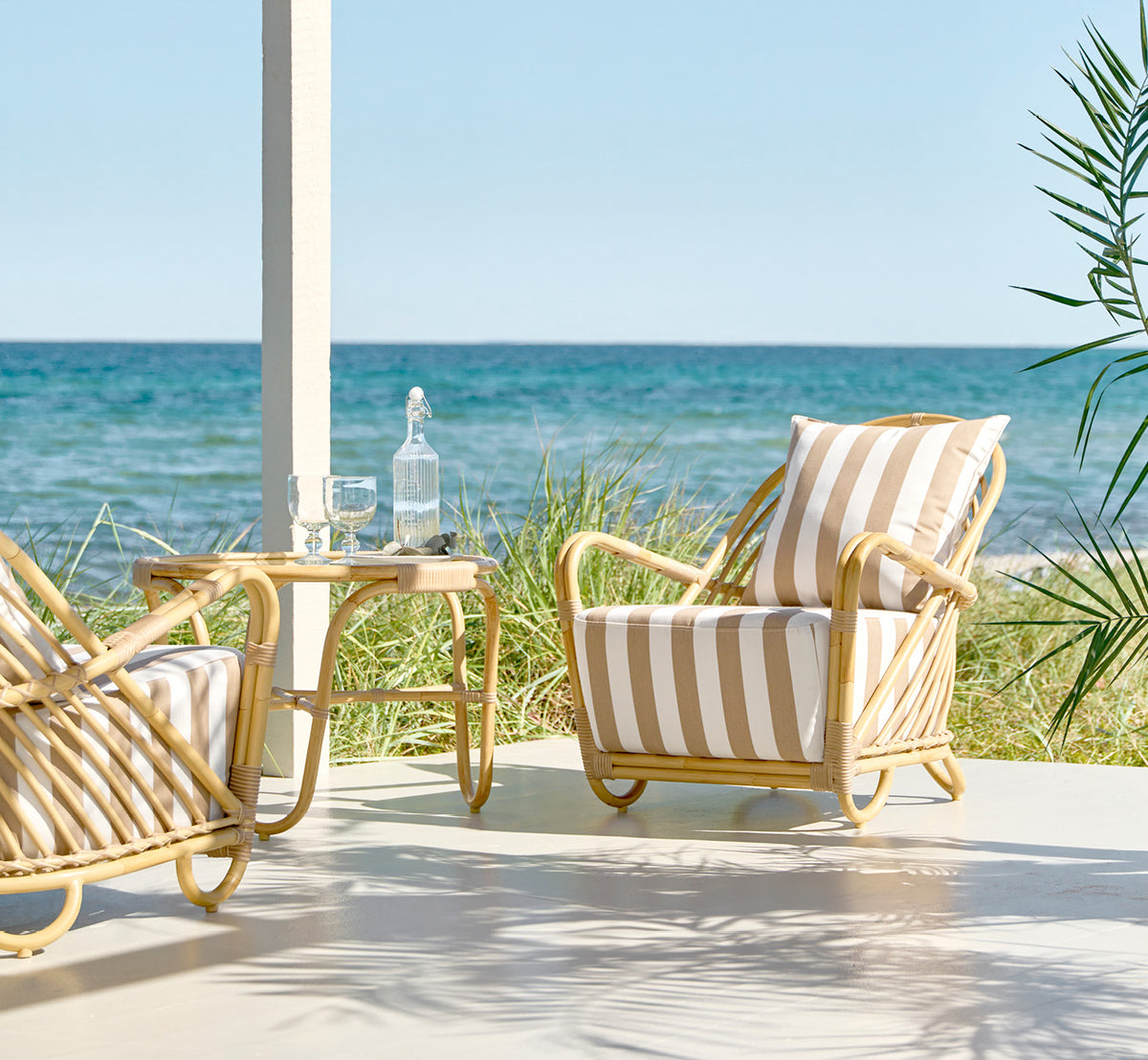 Esta es una imagen de estilo de vida de Charlottenborg sillón lounge exterior en natural Aluminium ArtFibre, en una terraza de madera al aire libre.