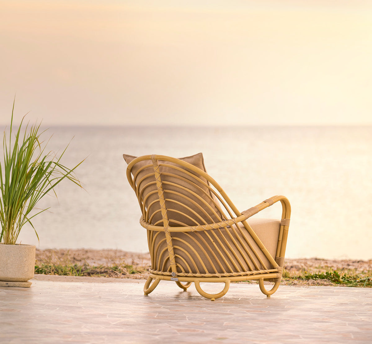 Esta es una imagen de estilo de vida de Charlottenborg sillón lounge exterior en natural Aluminium ArtFibre, en una terraza de madera al aire libre.