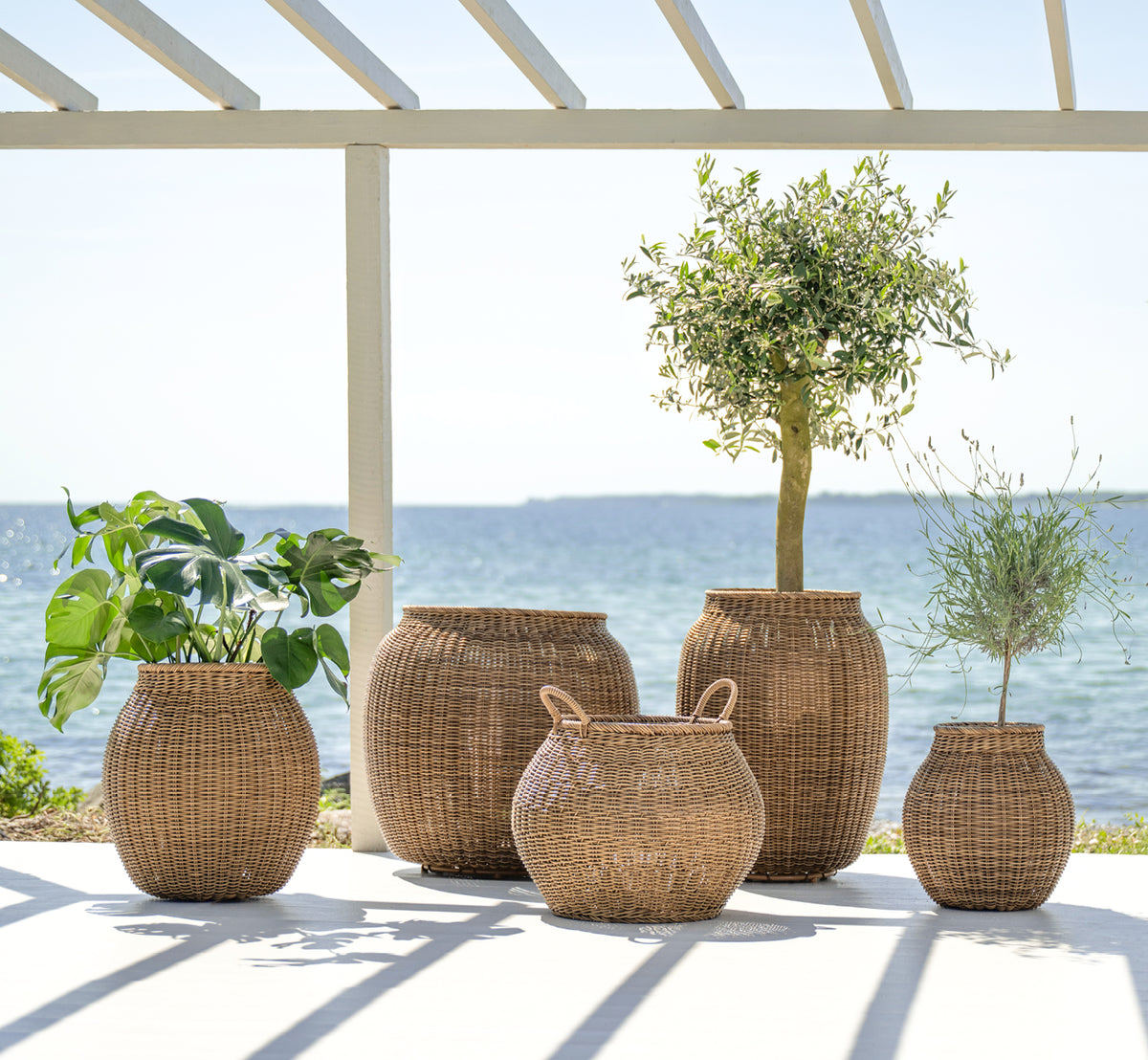 Esta es una imagen de estilo de vida de Ellis cesta en chestnut core weave ArtFibre Aluminium, en un patio exterior soleado con pared blanca y suelo.