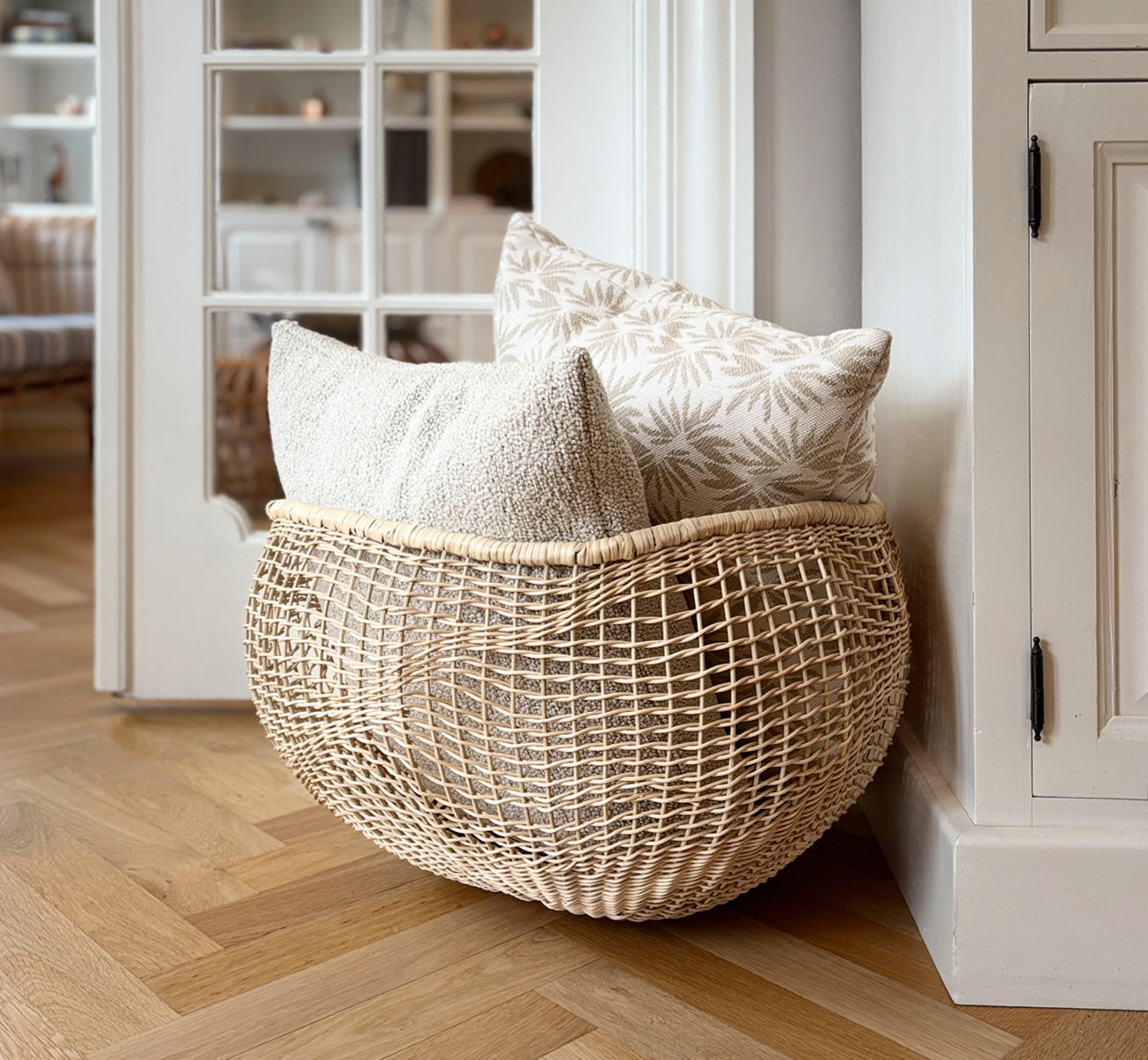 Esta es una imagen de estilo de vida de Folia cesta en natural core weave iron frame, en un interior blanco y luminoso con revestimiento de pared,.