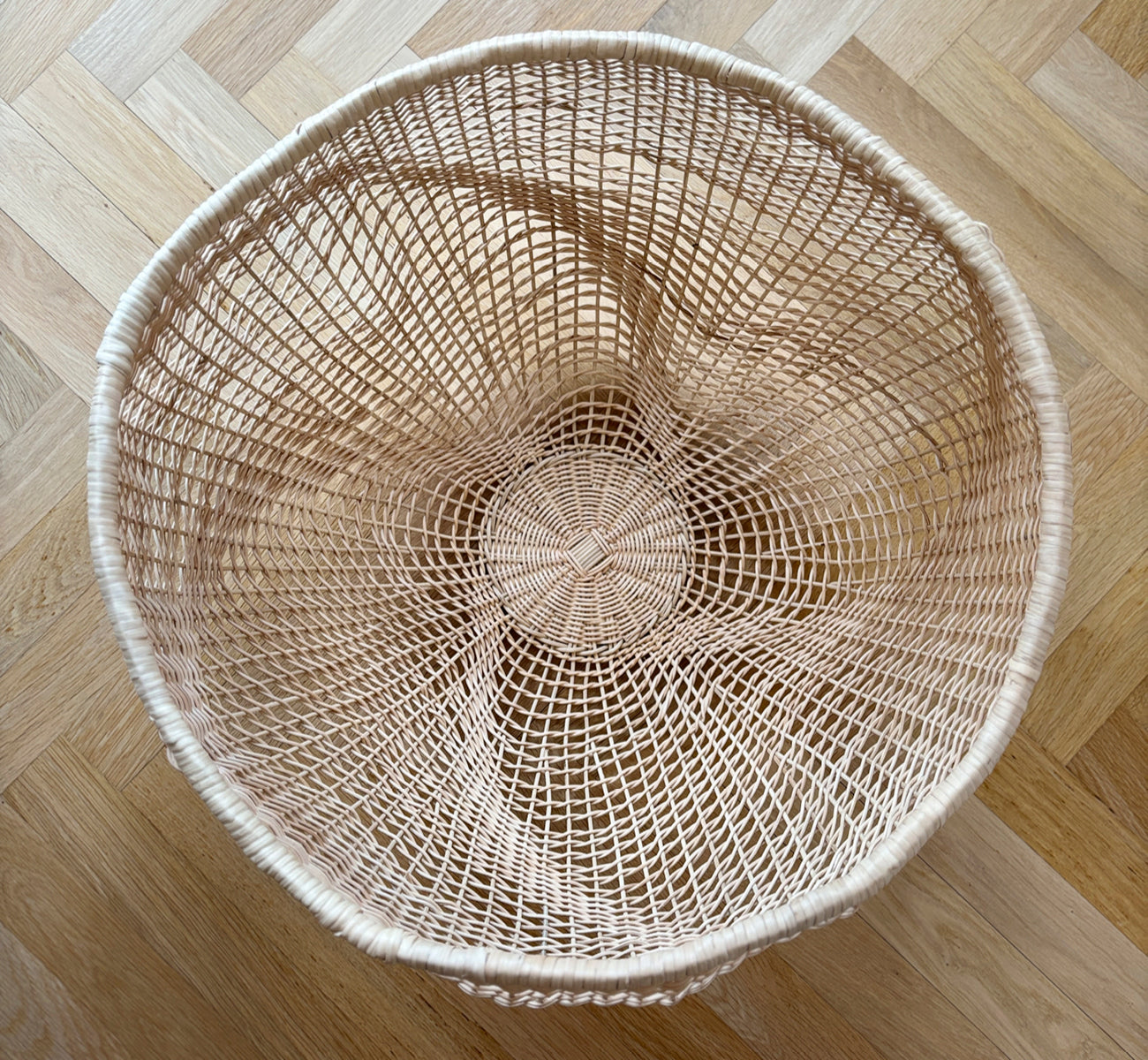 Esta es una imagen de estilo de vida de Folia cesta en natural core weave iron frame, en un interior blanco y luminoso con revestimiento de pared,.