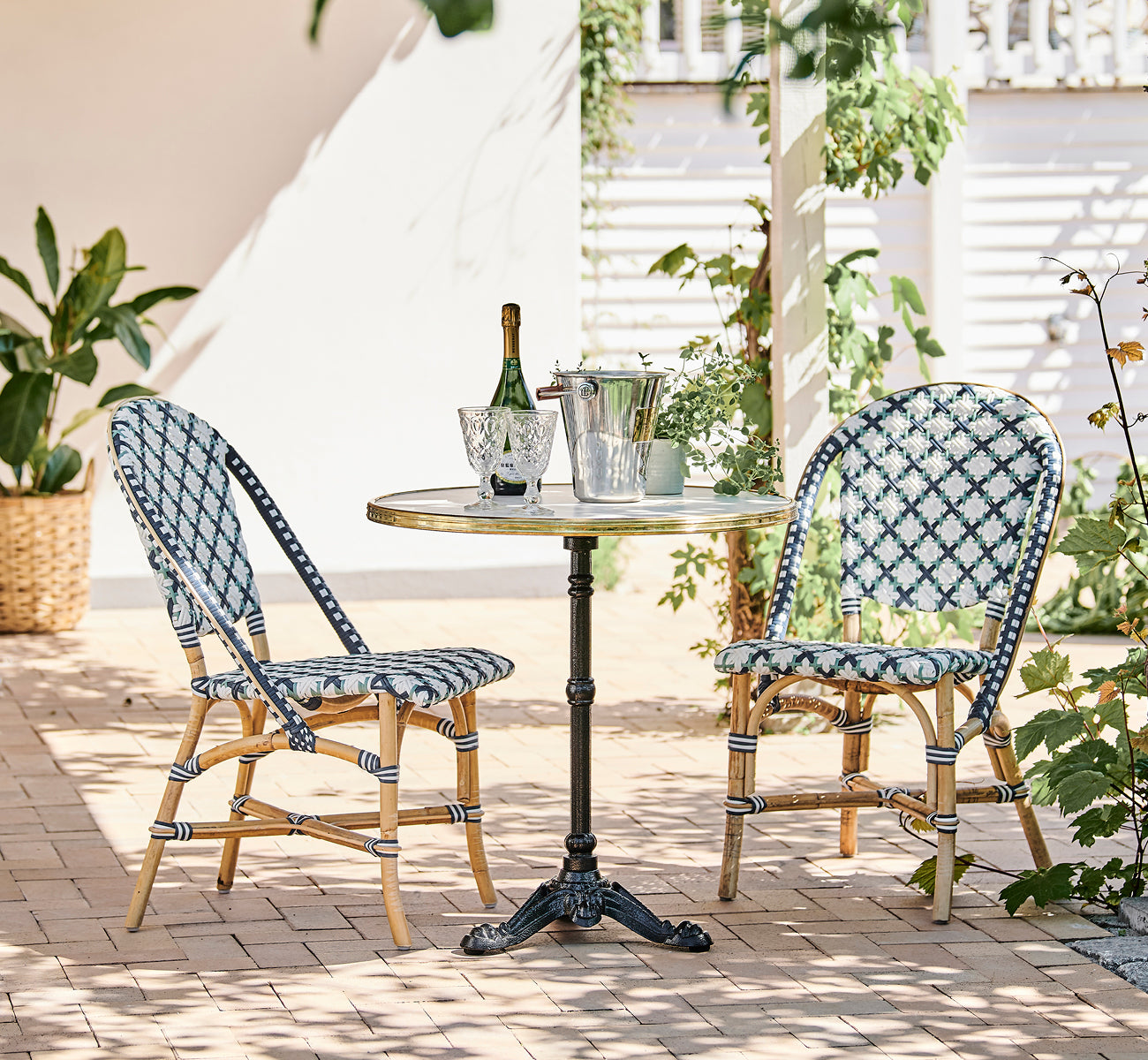 Esta es una imagen de estilo de vida de Lyon mesa de café Versalite Marble Ø70 cm en cast iron. Terraza soleada con sillas de bistró y una botella de champán.