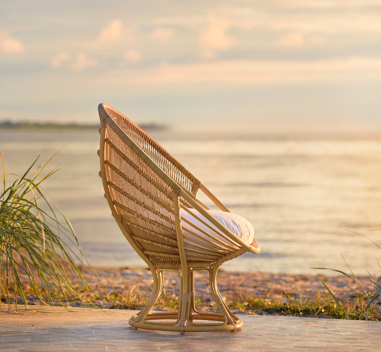 Esta es una imagen de estilo de vida de Luna sillón lounge exterior en natural aluminium artfibre. Colocada en la orilla al atardecer dorado con el océano detrás.