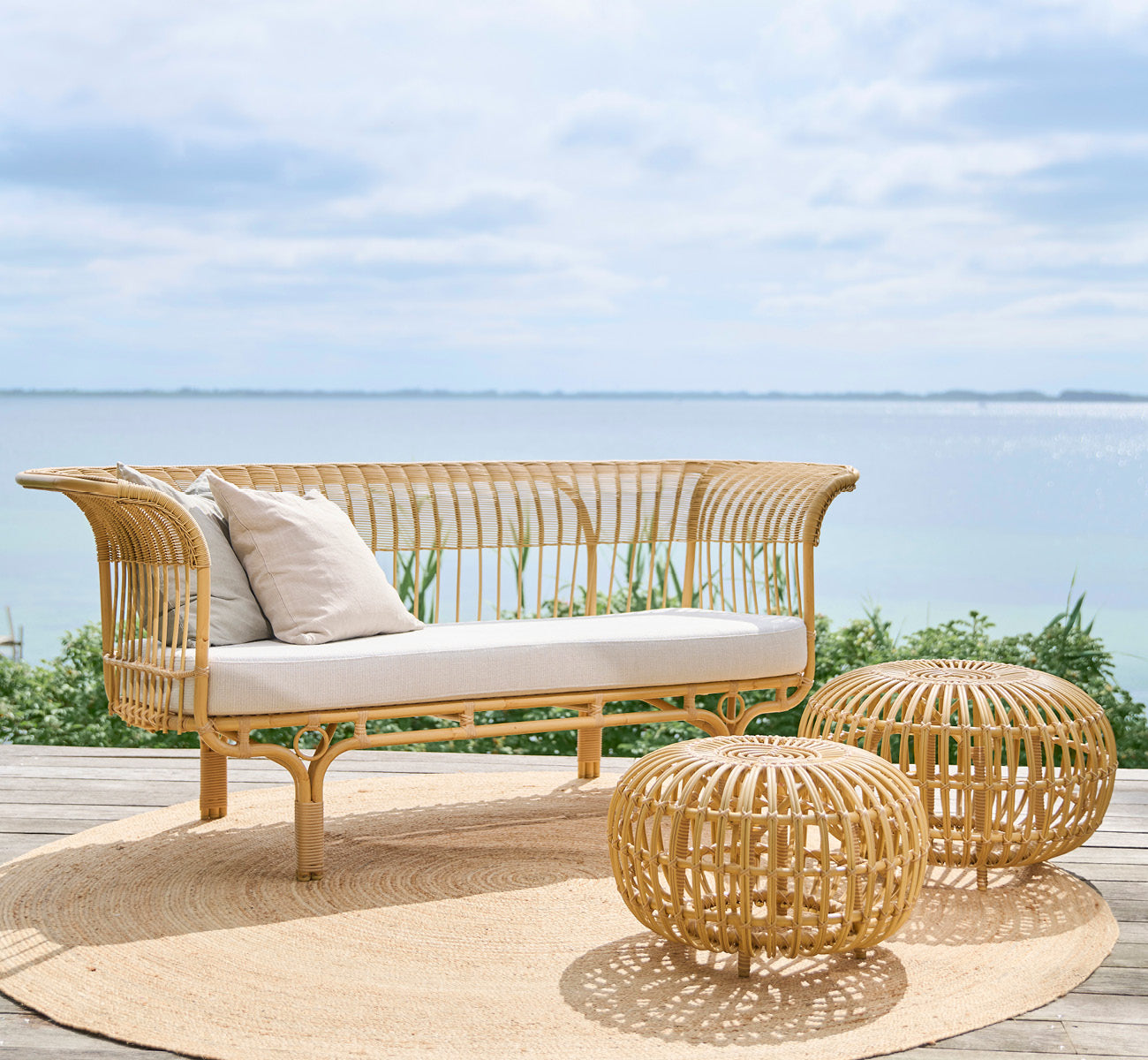 Esta es una imagen de estilo de vida de Belladonna sofá exterior en natural Aluminium ArtFibre, en una terraza de madera al aire libre con vistas al.
