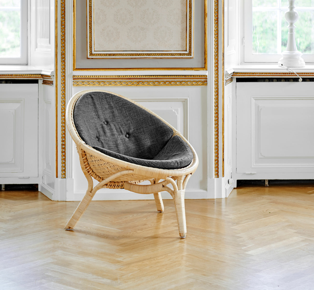 Esta es una imagen de estilo de vida de Rana sillón lounge en natural core weave rattan frame. De pie sola en una sala con paneles dorados y suelo de parqué.