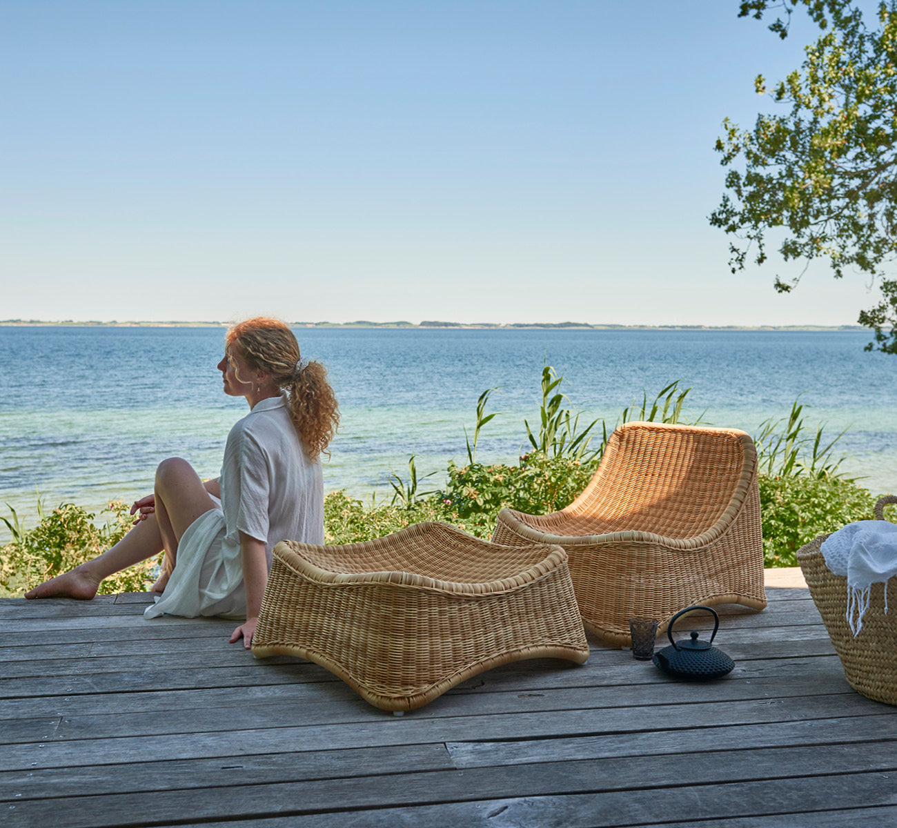 Esta es una imagen de estilo de vida de Chill sillón lounge en natural core weave ArtFibre Aluminium, en una terraza de madera junto al agua con.