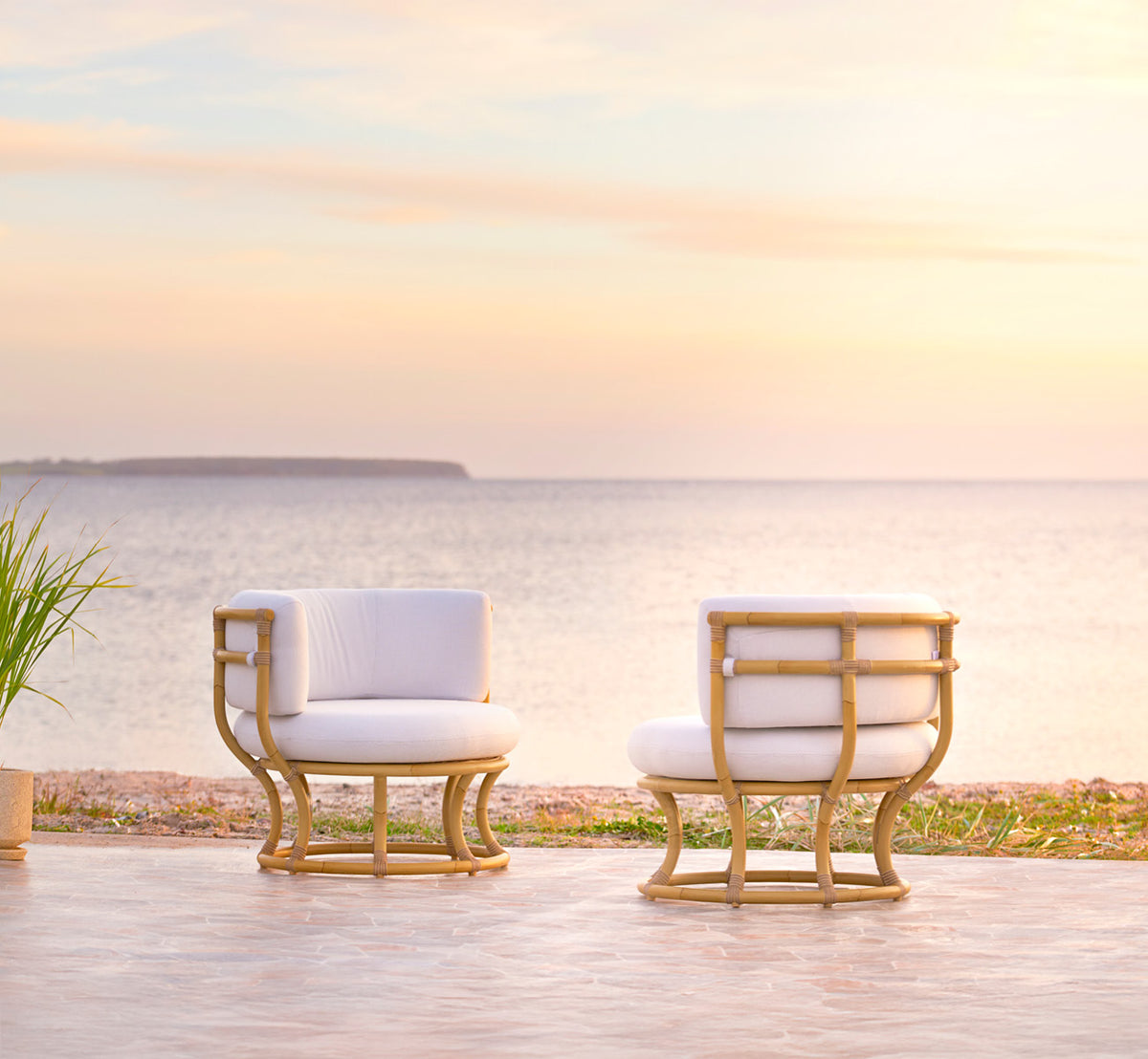 Esta es una imagen de estilo de vida de Coco sillón lounge exterior en natural Aluminium ArtFibre, en una terraza costera abierta al atardecer con.