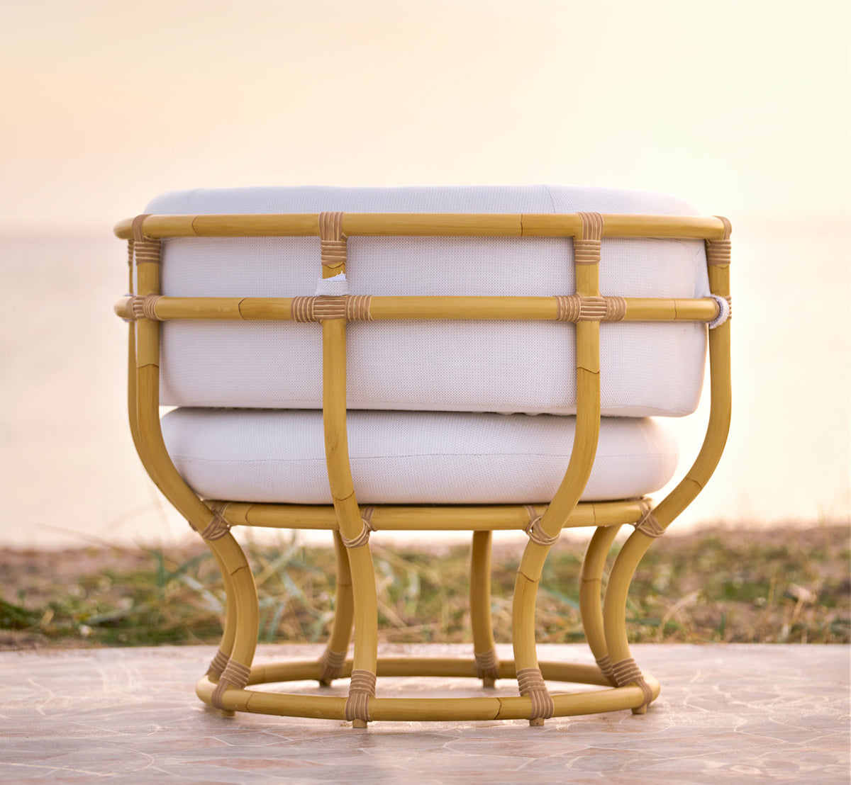 Esta es una imagen de estilo de vida de Coco sillón lounge exterior en natural Aluminium ArtFibre, en una terraza costera abierta al atardecer con.