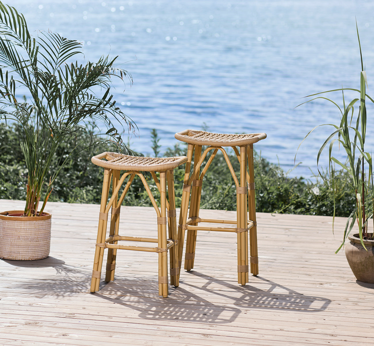 Esta es una imagen de estilo de vida de Salsa taburete alto de bar exterior en natural aluminium artfibre. Terraza frente al mar con palmeras y vista al océano.